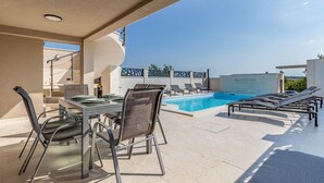 Un espace piscine aménagé sur le toit, avec une table et des chaises, des chaises longues et une vue dégagée sur le ciel.