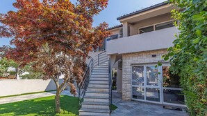 Une maison moderne à deux étages, dotée d’un escalier en pierre menant à une entrée avec porte en verre.