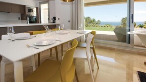 Een eetruimte met een witte tafel gedekt voor vier personen, gele stoelen en uitzicht op de oceaan door grote ramen.