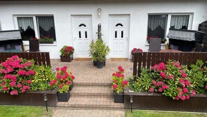 A white house with a red-tiled roof, two white doors, and a brick pathway leading to a wooden bench. - Apartment Denise (M) - Kölp - Labahn (Loddin)