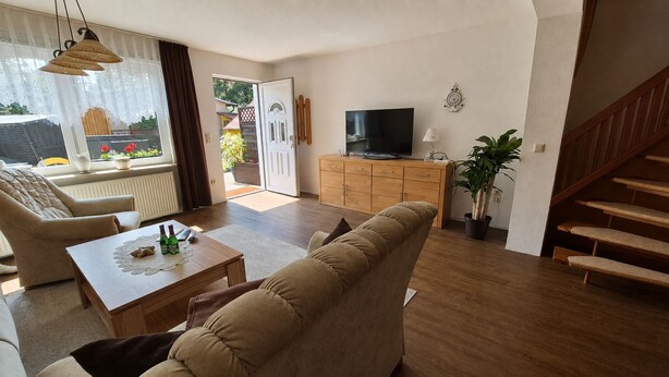 A living room with a sofa, a coffee table, a TV on a wooden cabinet, a potted plant, and a staircase. - Apartment Denise (M) - Kölp - Labahn (Loddin)