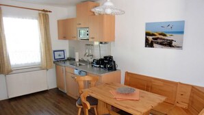 A compact kitchen with a microwave, coffee maker, and a small dining area with wooden furniture. - Apartment Denise (M) - Kölp - Labahn (Loddin)