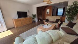 A living room with a sofa, a coffee table, a TV, a staircase, and a plant. - Apartment Denise (M) - Kölp - Labahn (Loddin)