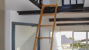 Eine Holzleiter in einem Raum mit weißen Wänden und einem schwarzen Deckenbalken.