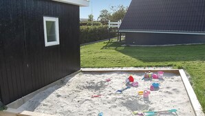 Ein Sandkasten mit verschiedenen Spielsachen und einer hölzernen Konstruktion mit Fenster.
