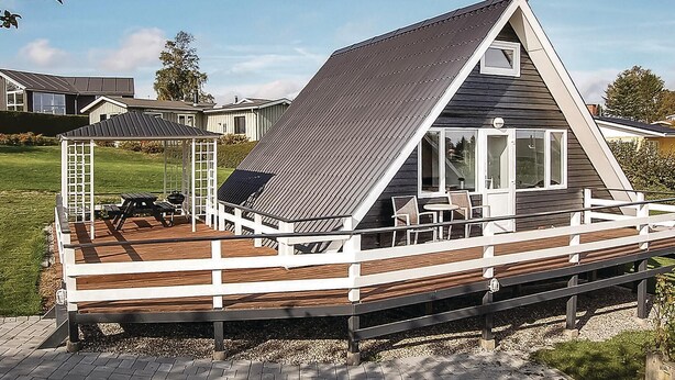 Ein modernes Haus mit einer großen Terrasse, einer überdachten Veranda und einem markanten, dreieckigen Dach.