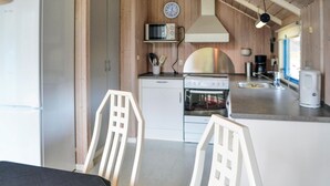 A compact kitchen with white cabinets, a microwave, a stove, and a sink. There are two white chairs in the foreground. - 3 bedroom cozy home in Oksbøl (Oksbøl)