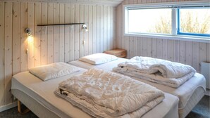 A room with two beds, a small bedside table, a window with a view of trees, and wooden walls. - 3 bedroom cozy home in Oksbøl (Oksbøl)