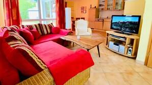 Ein Wohnzimmer mit einem roten Sofa, einem weißen Sessel, einem Holztisch und einem Fernseher auf einem Holzschrank.