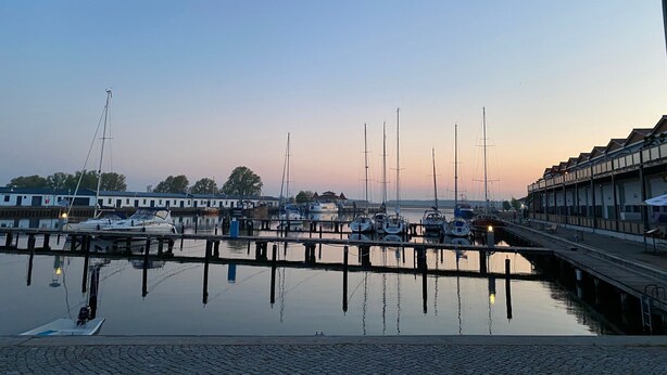 Ein Yachthafen mit mehreren angedockten Booten, einer hölzernen Pier und einem Gebäude mit Balkon.