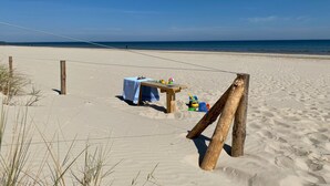 Ein Sandstrand mit einem Holztisch, Stühlen, einer Seilsperre und einer Holzkonstruktion.