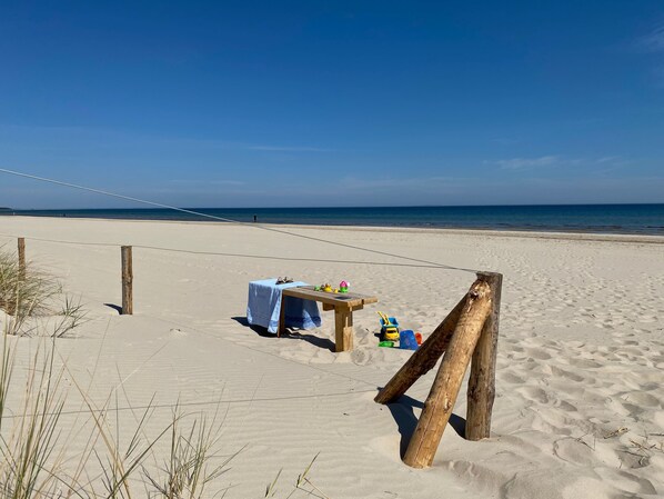 Una playa arenosa con una pequeña mesa de madera cubierta con un mantel, un banco y algunos juguetes.