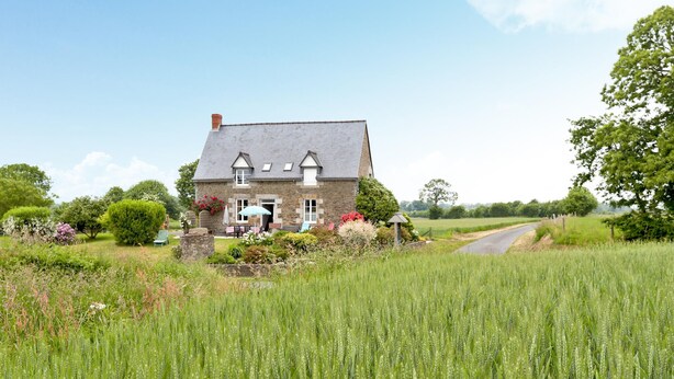 Een stenen huis met een schuin dak, een zichtbare schoorsteen en een tuin vol planten en bloemen.