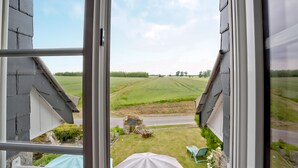 Uitzicht vanuit een raam met metalen kader, op een groen veld en een weg.