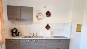 Une cuisine moderne avec des meubles gris, un évier en acier inoxydable, une machine à café et une horloge au mur.