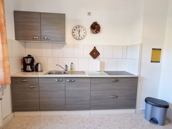 A modern kitchen with grey cabinets, a stainless steel sink, a coffee maker, and a clock on the wall.