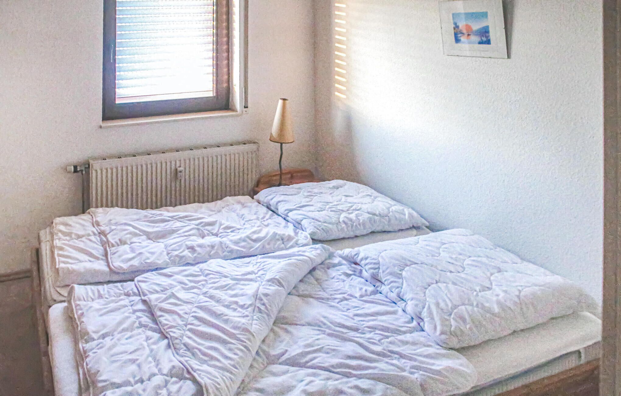 A bedroom with a single bed, a radiator, a window with blinds, and a picture on the wall.
