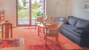 A living room with a grey sofa, wicker chairs, a red rug, and a view through a glass door to a balcony.