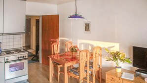 A compact kitchen with a stove, wooden dining table, chairs, and a TV.