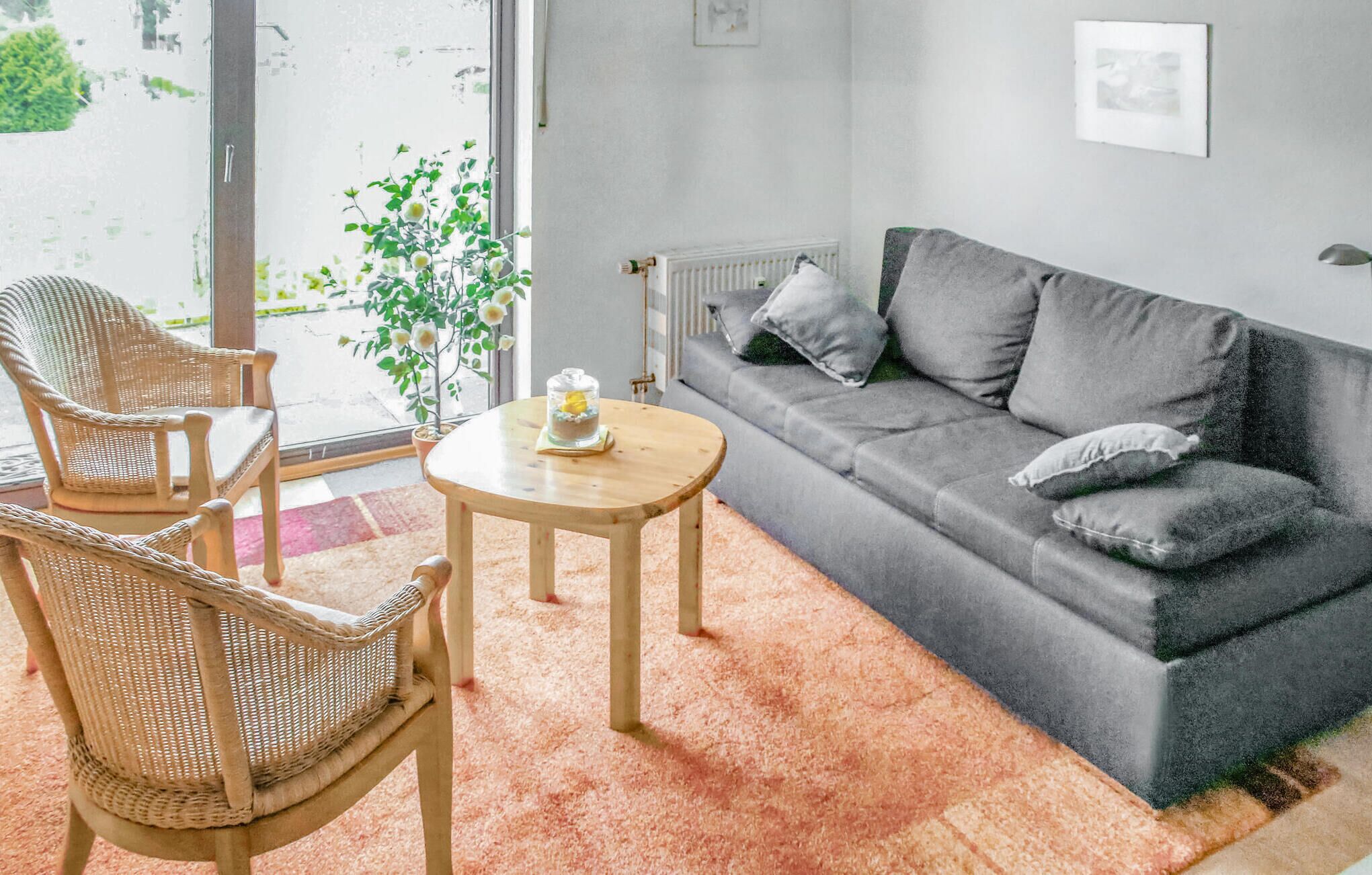 A living room with a grey sofa, two wicker chairs, a small round table, and a potted plant.