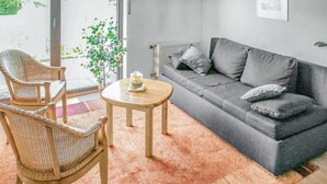 A living room with a grey sofa, two wicker chairs, a small round table, and a potted plant.