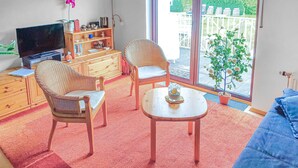 A living room with a TV, two wicker chairs, a small table, and a potted plant by a large window.