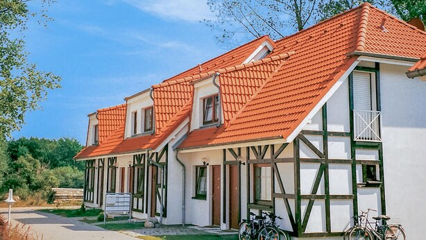 A traditional half-timbered house with a red-tiled roof, two visible windows, and a bicycle parked outside.