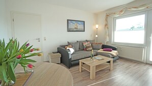 Ein Wohnzimmer mit einer Couch, einem Couchtisch, einer Tulpenvase und einem gerahmten Bild an der Wand.