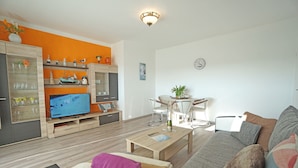 Ein modernes Wohnzimmer mit Fernseher, Holzmöbeln und einer leuchtend orangefarbenen Wand.