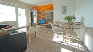 Ein modernes Wohnzimmer mit einer Couch, einem Esstisch mit Stühlen, einem Fernseher und einer Küchenzeile mit Schränken und einem Herd.