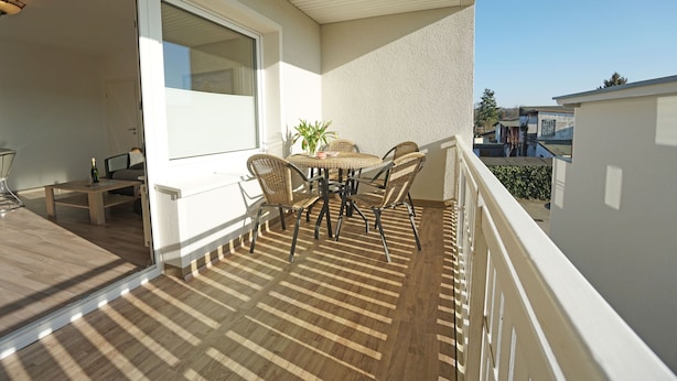 Ein Balkon mit Holztisch und -stühlen, einem Blumentopf und Blick auf benachbarte Gebäude.