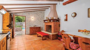 A rustic kitchen with a stone wall, wooden cabinets, a brick oven, and a dining area with a table and chairs. - Gorgeous home in Reburici (Reburici)