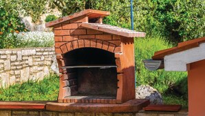 A brick-built outdoor pizza oven with a stone base, set against a stone wall and surrounded by greenery. - Gorgeous home in Reburici (Reburici)