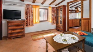 A cozy living room with a television, wooden furniture, a dining table with tea cups, and a kitchen visible through an open door. - Gorgeous home in Reburici (Reburici)