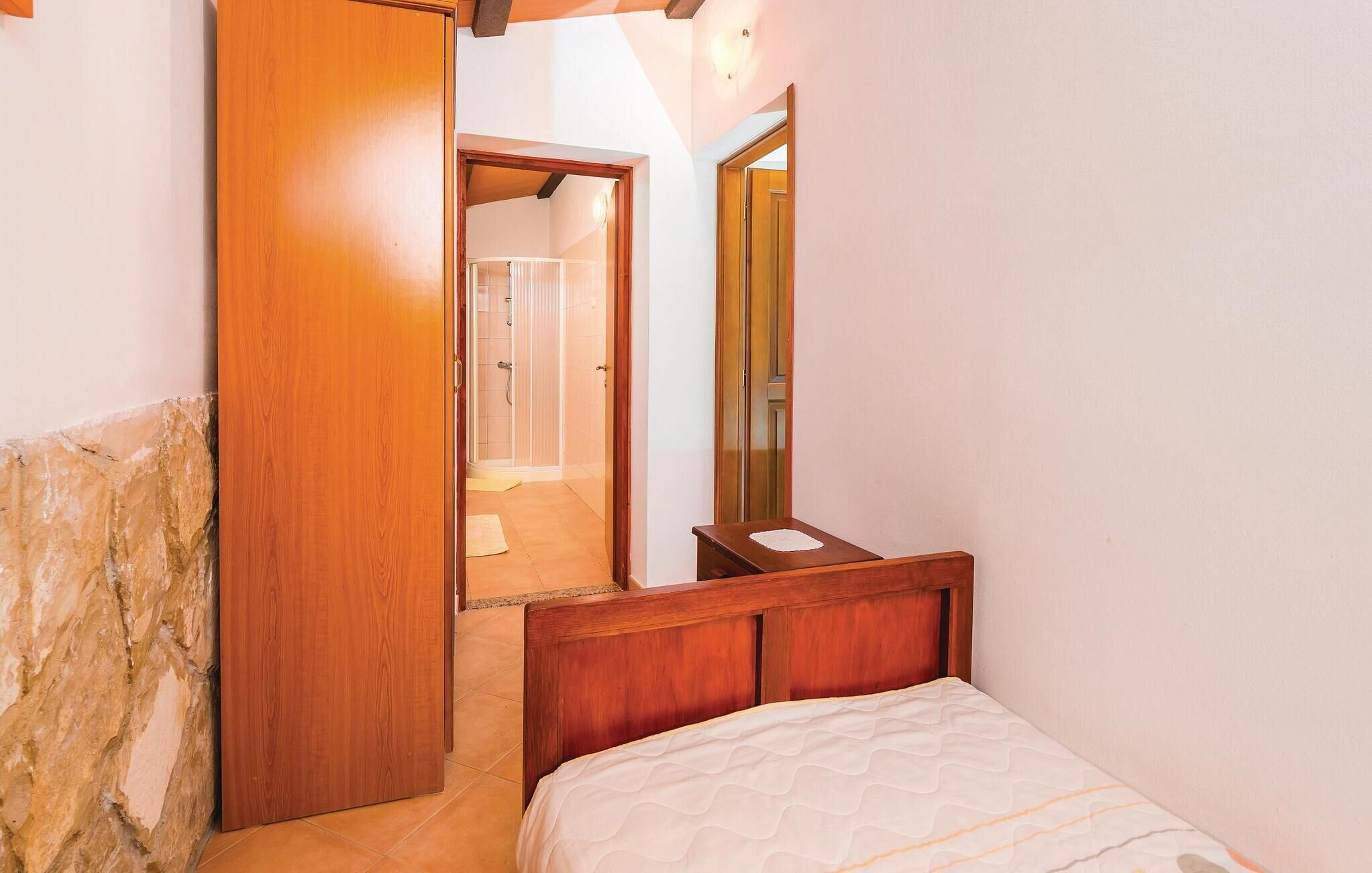 A bedroom with a wooden bed, a stone wall, and a bathroom visible through an open door.