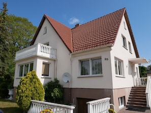 A two-story house with a red-tiled roof, white exterior walls, and a balcony.
