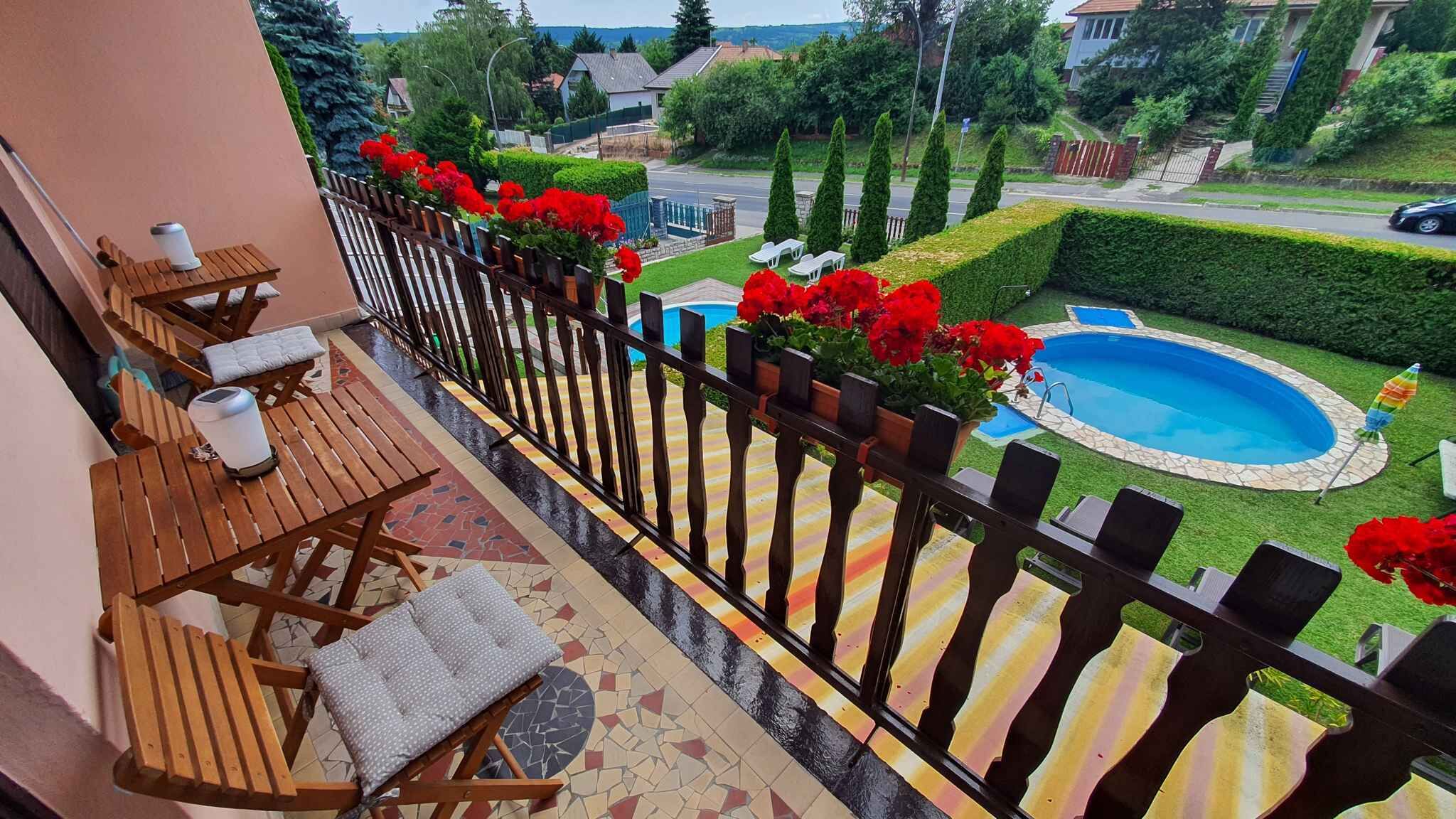 A balcony with wooden furniture, a pool, and a view of a residential area.