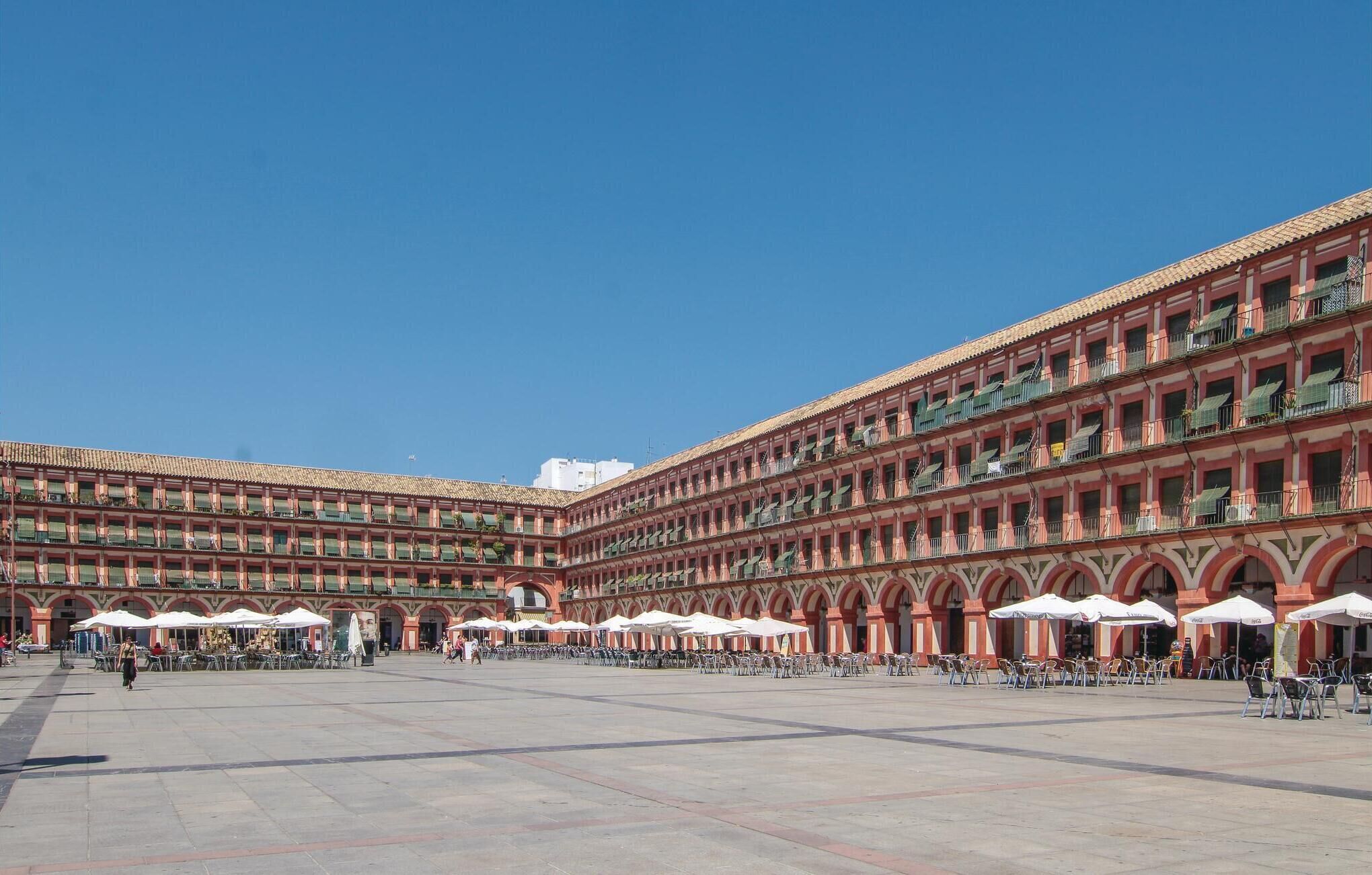 A spacious courtyard with multiple levels of balconies, outdoor seating areas, and a clear blue sky.