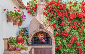 A rustic outdoor kitchen area with a brick oven, potted plants, and a metal rack. - Nice home in Córdoba with WiFi (Córdoba)