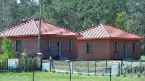 Two brick buildings with red-tiled roofs, surrounded by a fence and trees. - 2 bedroom lovely home in Glowczyce (Glowczyce)