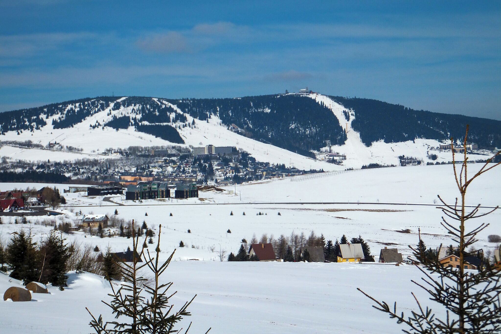 Un paysage enneigé avec une ville située dans la vallée et une montagne en arrière-plan.
