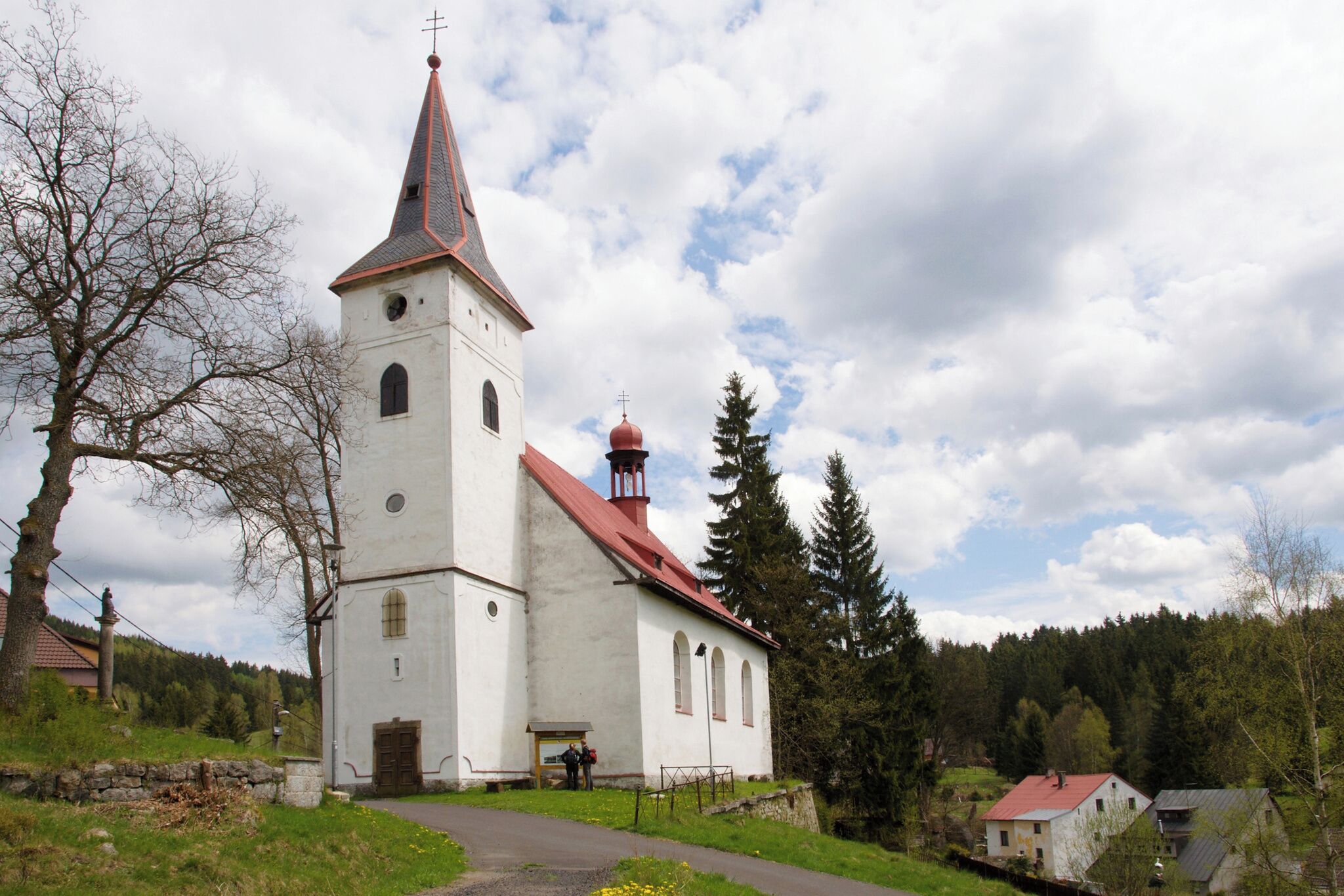 Una iglesia con un campanario alto y un techo rojo, rodeada de árboles y algunas casas.