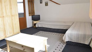 Een slaapkamer met twee bedden, een houten garderobe, een televisie en een klein tafeltje.