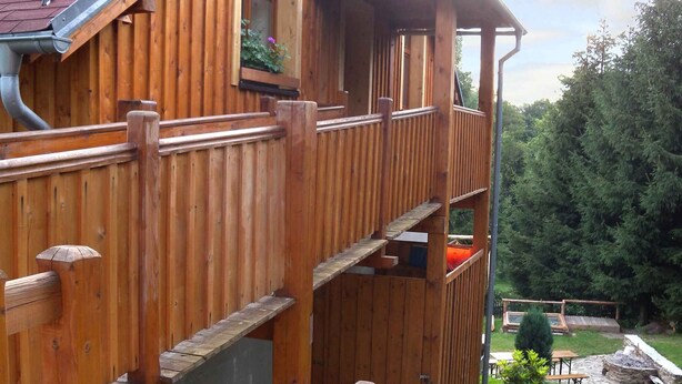 Een meerlaags houten gebouw met een schuin dak, een houten terras en een kleine tuin.