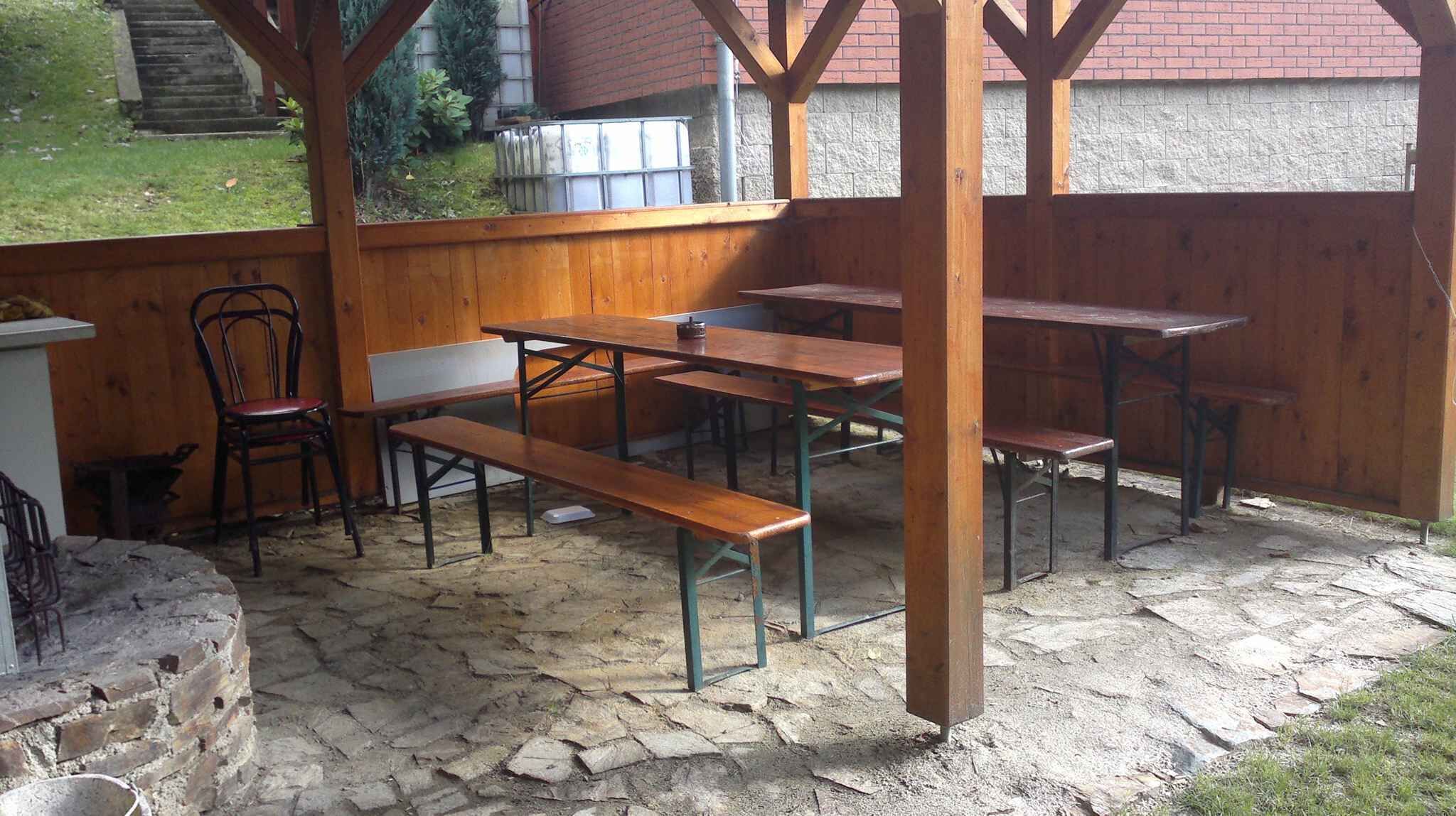 An outdoor patio with wooden tables and benches, stone flooring, and a brick wall in the background.
