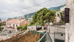 A residential area with stone walls, a tiled roof, and a view of a hill with buildings in the distance.