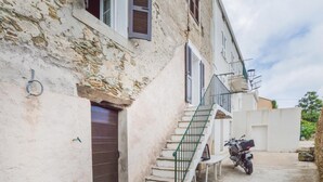 A narrow street with a building featuring a staircase, a door, and a motorcycle parked outside.