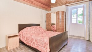 A bedroom with a wooden bed, a small wooden nightstand, a wardrobe, and a window with curtains.