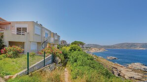 Ett bostadsområde vid kusten med moderna hus, fri utsikt över havet och en klippig strand.