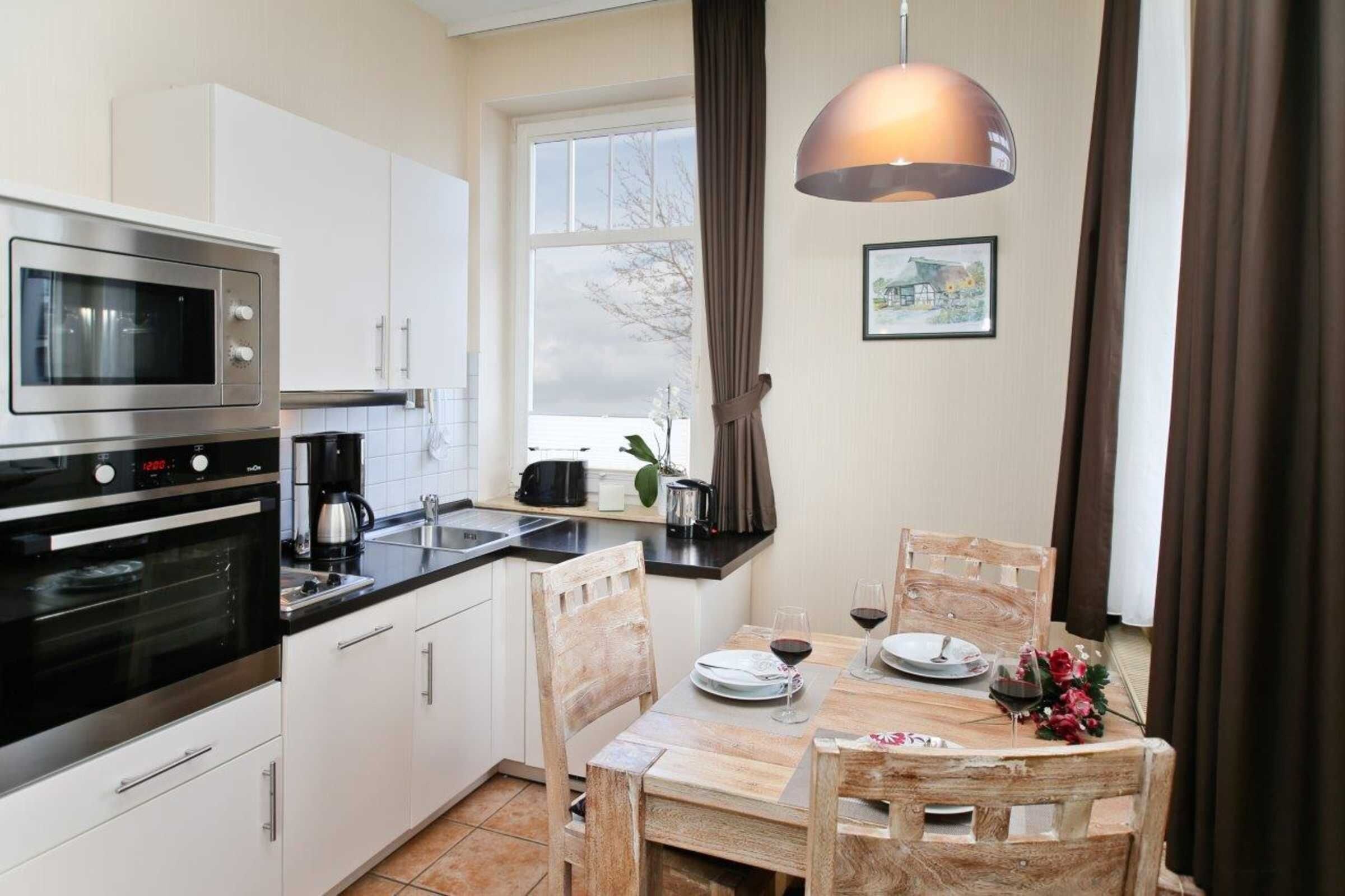 A modern kitchen with a microwave, oven, and coffee maker, a dining table with chairs, and a pendant light.